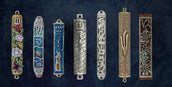 Assorted decorative mezuzah cases with floral, Hebrew, and artistic designs on a blue background