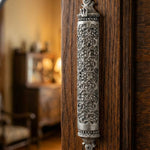 Traditional Mosaic Magen David Pewter Mezuzah, mounted vertically on a rustic wooden door in a warmly lit traditional Jewish home