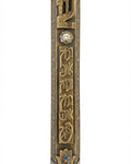 A detailed high-resolution image of an Ariel Brass Mezuzah with engraved Hebrew letters and decorative motifs, set against a pure white background with a soft reflection.