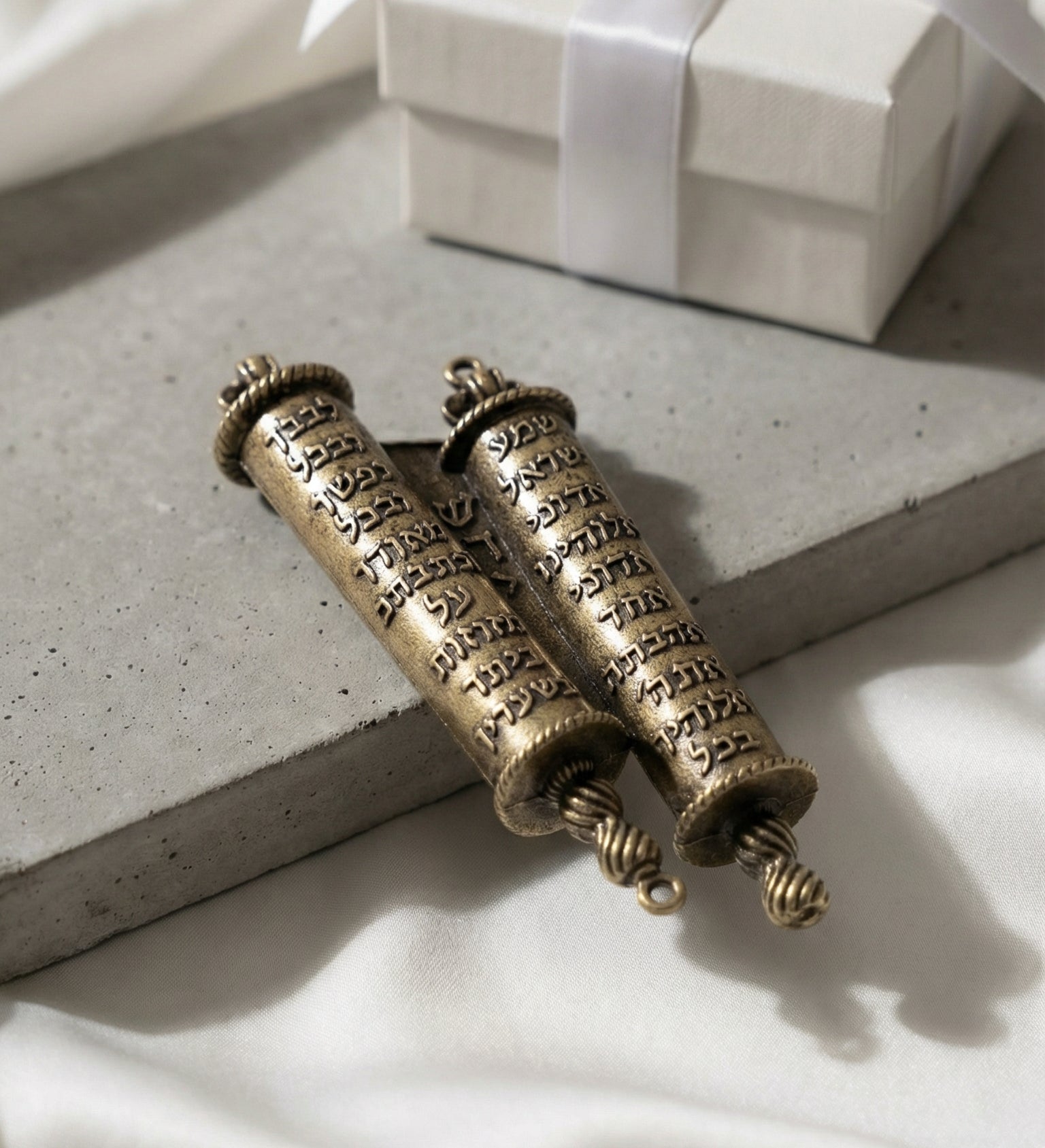 Brass Torah Mezuzah on matte concrete with white silk and gift box in soft diffuse light emphasizing craftsmanship and luxury.