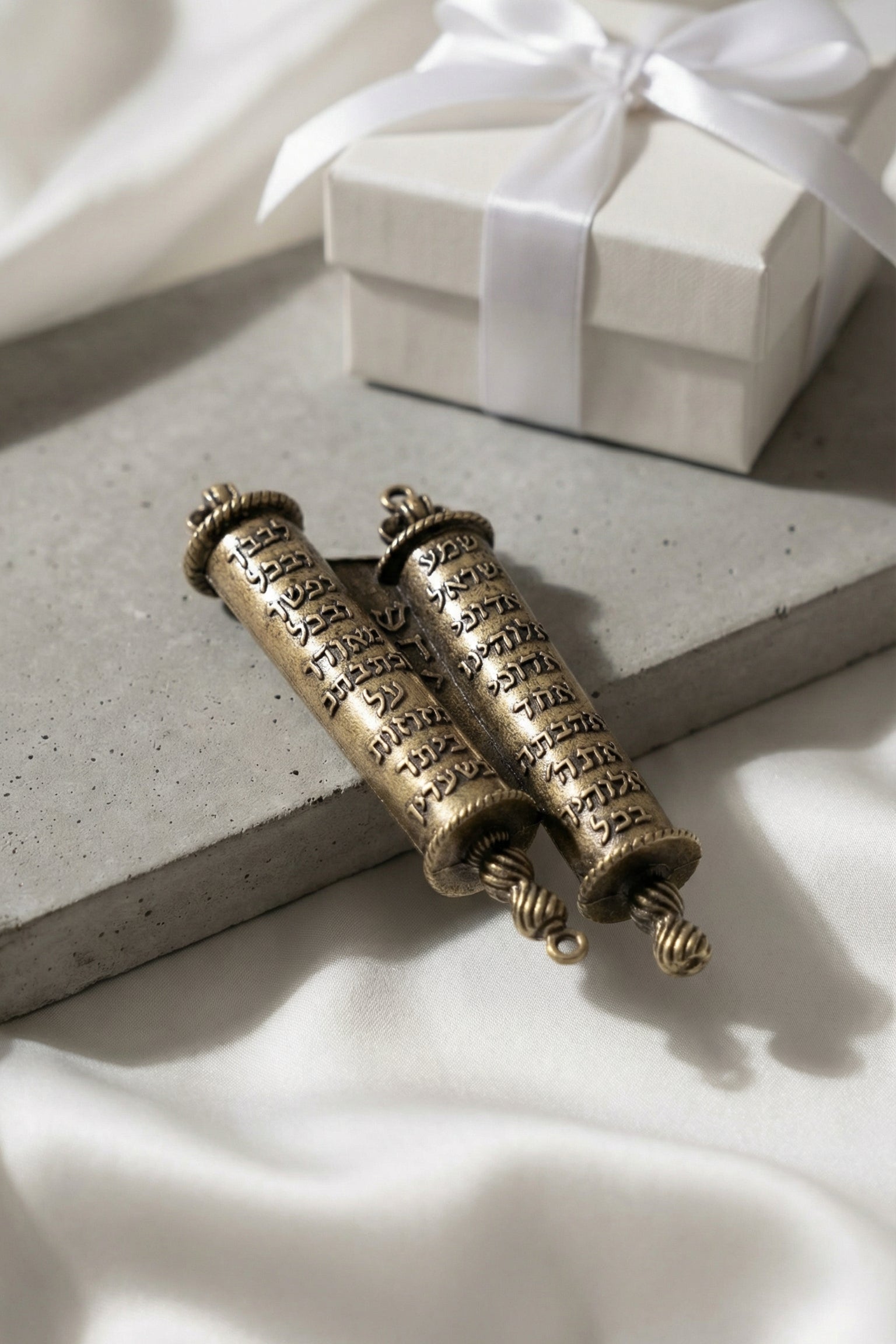 Brass Torah Mezuzah on matte concrete with white silk and gift box in soft diffuse light emphasizing craftsmanship and luxury.