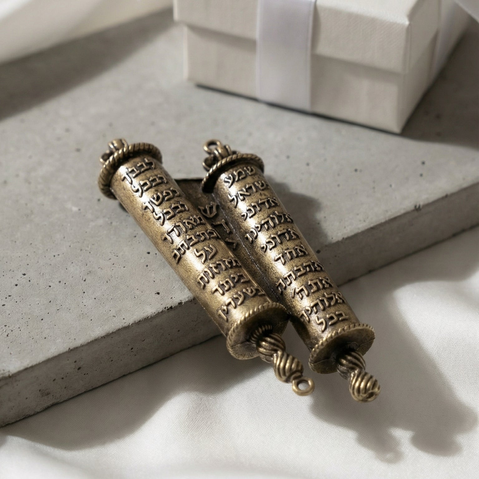 Brass Torah Mezuzah on matte concrete with white silk and gift box in soft diffuse light emphasizing craftsmanship and luxury.