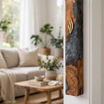 Olive wood and charcoal black resin mezuzah case mounted on a white doorpost next to a sunlit living room, its smoky gray resin, warm olive wood grain and gold Shin shown at true size on a home entrance