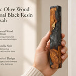 Hand holding a 7.5-inch olive wood and charcoal resin mezuzah case with gold Shin detail against a soft neutral background.