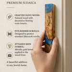 Person holding an artistic olive wood mezuzah with ocean blue and turquoise resin and a gold-toned Shin symbol.