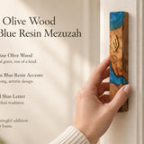 Hand holding a 7.5-inch artistic mezuzah case crafted from olive wood and blue ocean resin with a gold Shin letter.