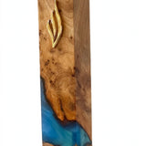 Angled view of the Artistic Olive Wood Ocean Blue Resin Mezuzah, a handcrafted Israeli mezuzah case where natural olive wood grain meets swirling blue and turquoise resin under a gold Shin, made for a 6-inch kosher scroll