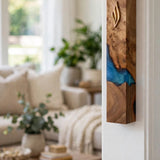 Artistic olive wood and ocean blue resin mezuzah mounted on a white doorframe beside a bright living room, showing how this handcrafted Israeli olive wood mezuzah case with a gold Shin looks at real doorpost scale