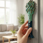 Hand applying Avatar Mezuzah to interior door, emphasizing size, texture, and craftsmanship in a minimalist home setting.