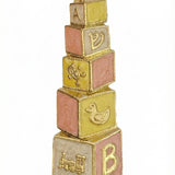 Hand-painted brass baby mezuzah in pink and yellow, 4 inches tall with Hebrew inscription, designed for nursery decor, with a bright white background.
