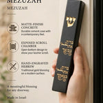 Person holding a black concrete mezuzah with gold Hebrew engraving featuring a blessing for the home entrance.