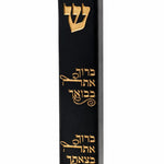the Baruch Atah Blessed Black Concrete Mezuzah case on a white background, showing its smooth black face, engraved gold Shin, and two engraved Hebrew lines blessing arrival and departure