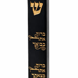 the Baruch Atah Blessed Black Concrete Mezuzah case on a white background, showing its smooth black face, engraved gold Shin, and two engraved Hebrew lines blessing arrival and departure