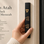 Person holding a black concrete mezuzah with gold Hebrew engraving in a bright, neutral-toned editorial setting.