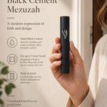 Handheld modern black cement mezuzah case with a raised sculptural silver-tone Shin, shown beside product details to demonstrate the slim profile, matte cement finish, minimalist design