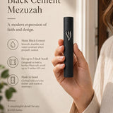 Handheld modern black cement mezuzah case with a raised sculptural silver-tone Shin, shown beside product details to demonstrate the slim profile, matte cement finish, minimalist design