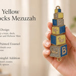 A hand holds a colorful, blue and yellow baby blocks mezuzah case featuring alphabet and toy decorations for a nursery