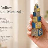 A hand holds a colorful, blue and yellow baby blocks mezuzah case featuring alphabet and toy decorations for a nursery