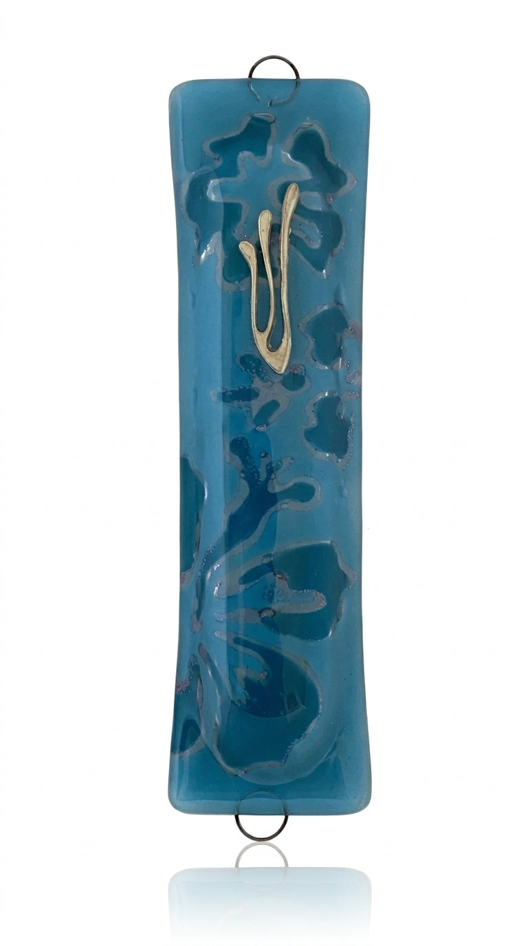 Blue glass mezuzah with detailed Hebrew inscriptions, engraved motifs, and textured surface, displayed on a clean white background with subtle reflection.