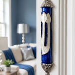 Heavenly Blue mezuzah case with luminous pearl design and deep blue enamel background mounted on a doorway in an indoor setting.