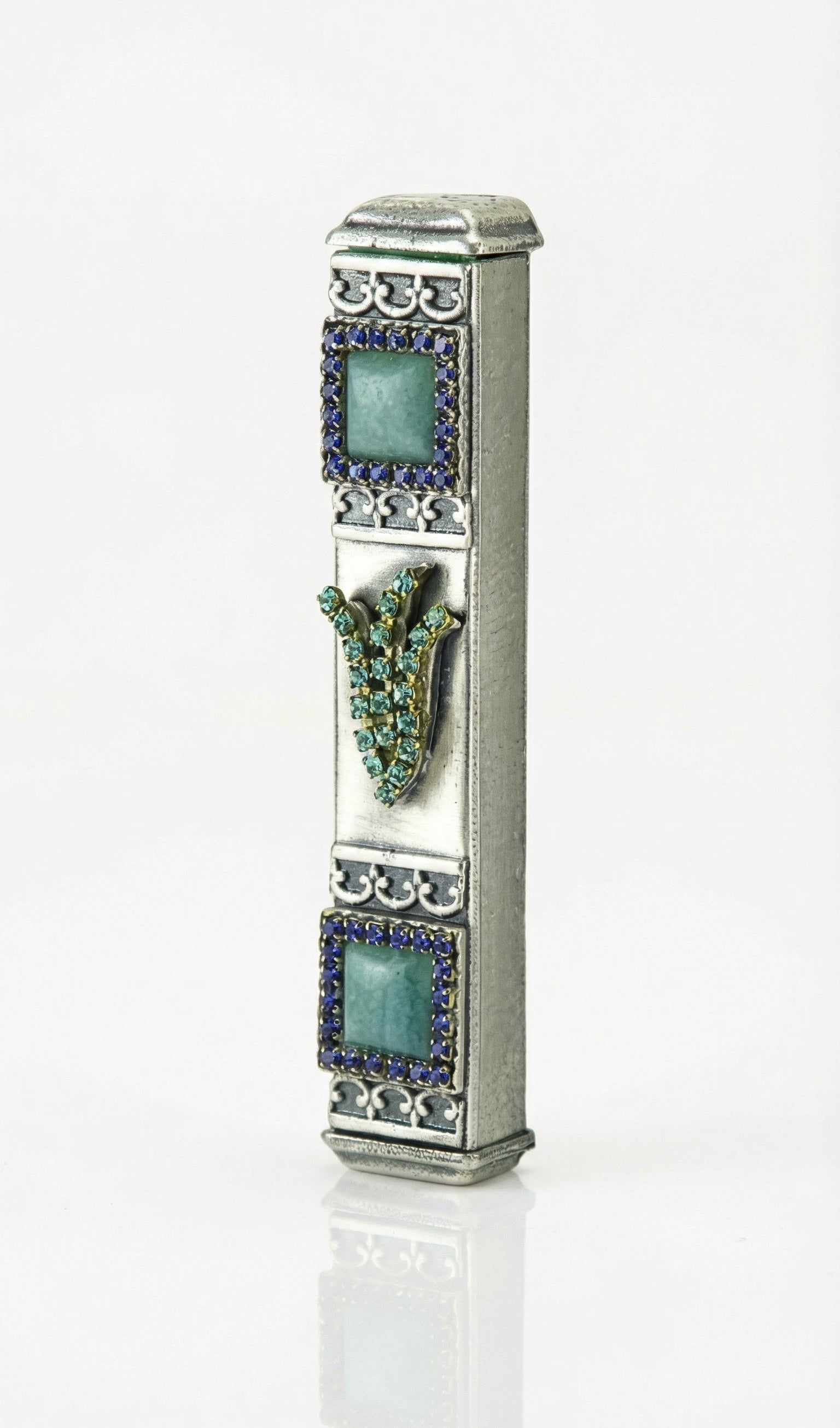Petite blue stone mezuzah with Hebrew shin and sparkling accents, on a polished white studio surface with a subtle reflection, showcasing detailed craftsmanship.