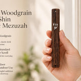 A person holds a brown woodgrain-look acrylic mezuzah with a silver crown and Shin, presented in an editorial lifestyle style.