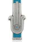 Blue Hamsa shaped Mezuzah with a central eye symbol, accented with silver and blue sparkling paint, placed on a white studio surface with soft reflection.