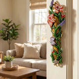 Colorful flowers and vines brass mezuzah with accent stones, mounted on a doorframe in an indoor lifestyle scene.