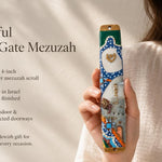 Hand-held display of colorful Kotel Gate mezuzah with vibrant Old City design, gold Shin, blue arched frame, and stone wall scene for doorway decoration.