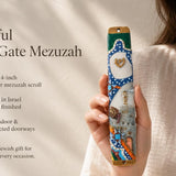 Hand-held display of colorful Kotel Gate mezuzah with vibrant Old City design, gold Shin, blue arched frame, and stone wall scene for doorway decoration.