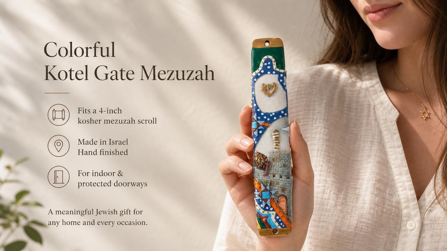 Hand-held display of colorful Kotel Gate mezuzah with vibrant Old City design, gold Shin, blue arched frame, and stone wall scene for doorway decoration.