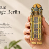 Die Neue Synagoge Berlin Mezuzah mezuzah cover held upright in one hand, showing golden ochre Fimo polymer clay shaped as the Berlin synagogue facade, with gray domes, tall windows and fine architectural relief beside the product name and illustrated design features in a wide social-sharing graphic for decorative Jewish home Judaica