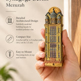Handheld portrait of the Die Neue Synagoge Berlin Mezuzah mezuzah cover, with golden ochre Fimo polymer clay shaped as the Berlin synagogue facade, with gray domes, tall windows and architectural relief clearly visible beside the product name and illustrated features of this distinctive Jewish doorway design