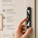 Person naturally holding the exact mezuzah in a refined editorial style with editorial text on the side, in a 9:16 premium presentation.