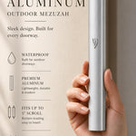 Handheld view of the sleek silver aluminum mezuzah, balanced with editorial text, showcasing its modern design and refined finish.