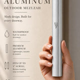 Handheld view of the sleek silver aluminum mezuzah, balanced with editorial text, showcasing its modern design and refined finish.