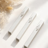 Three Eternal Flame silver aluminum mezuzah cases arranged on a warm neutral surface with dried florals, featuring raised silver ner tamid and stylized Shin emblems