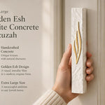 Person holding an extra large white concrete mezuzah with a gold flame-like Shin letter design.