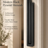 Extra Large Modern Black Pyramid Mezuzah mounted on a pale doorpost beside its product name and illustrated design features, showing the deep matte black aluminum mezuzah cover and three stepped bars as a minimalist detail for a Jewish home entrance