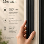Extra Large Modern Black Pyramid Mezuzah held beside a doorpost, with the deep matte black aluminum mezuzah cover shown close enough to reveal its three stepped bars and rounded lower edge alongside product-name and design callouts for this minimalist Judaica piece