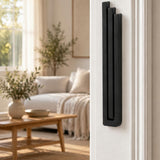 Extra Large Modern Black Pyramid Mezuzah mounted vertically on a white interior doorpost, where its deep matte black aluminum mezuzah cover and three graduated bars create a minimalist Judaica accent with clean geometric lines against the pale doorframe
