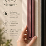 Extra Large Modern Burgundy Pyramid Mezuzah held beside a doorpost, with the muted burgundy wine-red aluminum mezuzah cover shown close enough to reveal its three stepped bars and rounded lower edge alongside product-name and design callouts for this minimalist Judaica piece