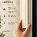 Extra Large Modern Cream Pyramid Mezuzah held beside a doorpost, with the warm ivory cream aluminum mezuzah cover shown close enough to reveal its three stepped bars and rounded lower edge alongside product-name and design callouts for this architectural Judaica piece
