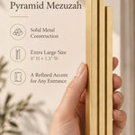 Hand holding the Extra Large Modern Gold Pyramid Mezuzah upright, revealing its warm metallic gold aluminum mezuzah cover, slender three-bar Pyramid design and graduated top beside illustrated product features for minimalist Jewish home Judaica
