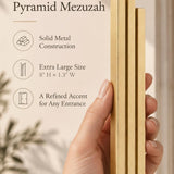 Hand holding the Extra Large Modern Gold Pyramid Mezuzah upright, revealing its warm metallic gold aluminum mezuzah cover, slender three-bar Pyramid design and graduated top beside illustrated product features for minimalist Jewish home Judaica
