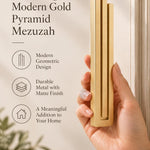 A hand presents the Extra Large Modern Gold Pyramid Mezuzah with its warm metallic gold aluminum mezuzah cover facing forward, highlighting the clean graduated bars and geometric vertical profile beside design illustrations for a minimalist Jewish doorway accent