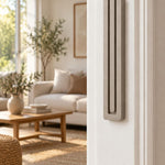 Extra Large Modern Sandstone Pyramid Mezuzah mounted vertically on a white interior doorpost, where its warm taupe sandstone aluminum mezuzah cover and three graduated bars create a minimalist Judaica accent with clean geometric lines against the pale doorframe