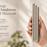 Extra Large Modern Sandstone Pyramid Mezuzah pictured in hand as a warm taupe sandstone aluminum mezuzah cover with three graduated bars and a minimalist stepped design, alongside its name and illustrated product features in a wide social-sharing image