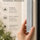 Extra Large Modern Silver Pyramid Mezuzah held beside a doorpost, with the softly brushed silver aluminum mezuzah cover shown close enough to reveal its three stepped bars and rounded lower edge alongside product-name and design callouts for this minimalist Judaica piece