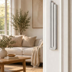 Extra Large Modern Silver Pyramid Mezuzah mounted vertically on a white interior doorpost, where its softly brushed silver aluminum mezuzah cover and three graduated bars create a minimalist Judaica accent with clean geometric lines against the pale doorframe